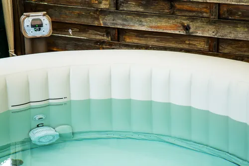 Spa gonflable rempli d'eau, avec son bloc de commande et de filtration, devant une palissade en bois