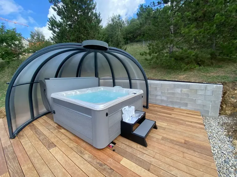 Spa installé par Sommum Wellness sous un abri bulle, sur une terrasse en bois, à Marvejols