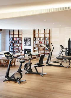 Une salle de sport à la maison : vélos, tapis de course et elliptique Technogym dans le séjour d’une villa, devant les bibliothèques