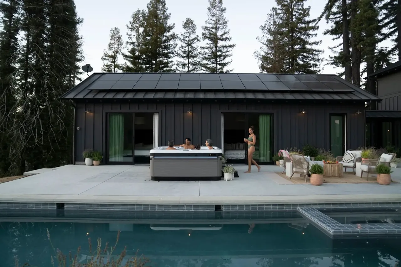 Spa Caldera occupé sur une terrasse en béton, devant une maison à bardage noir, piscine au premier plan