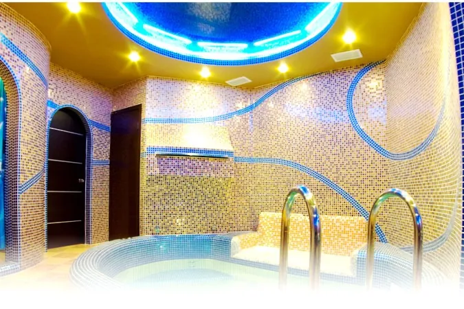 Hammam en mosaïque aux motifs bleus et dorés, arcs, voûte éclairée en bleu et bassin