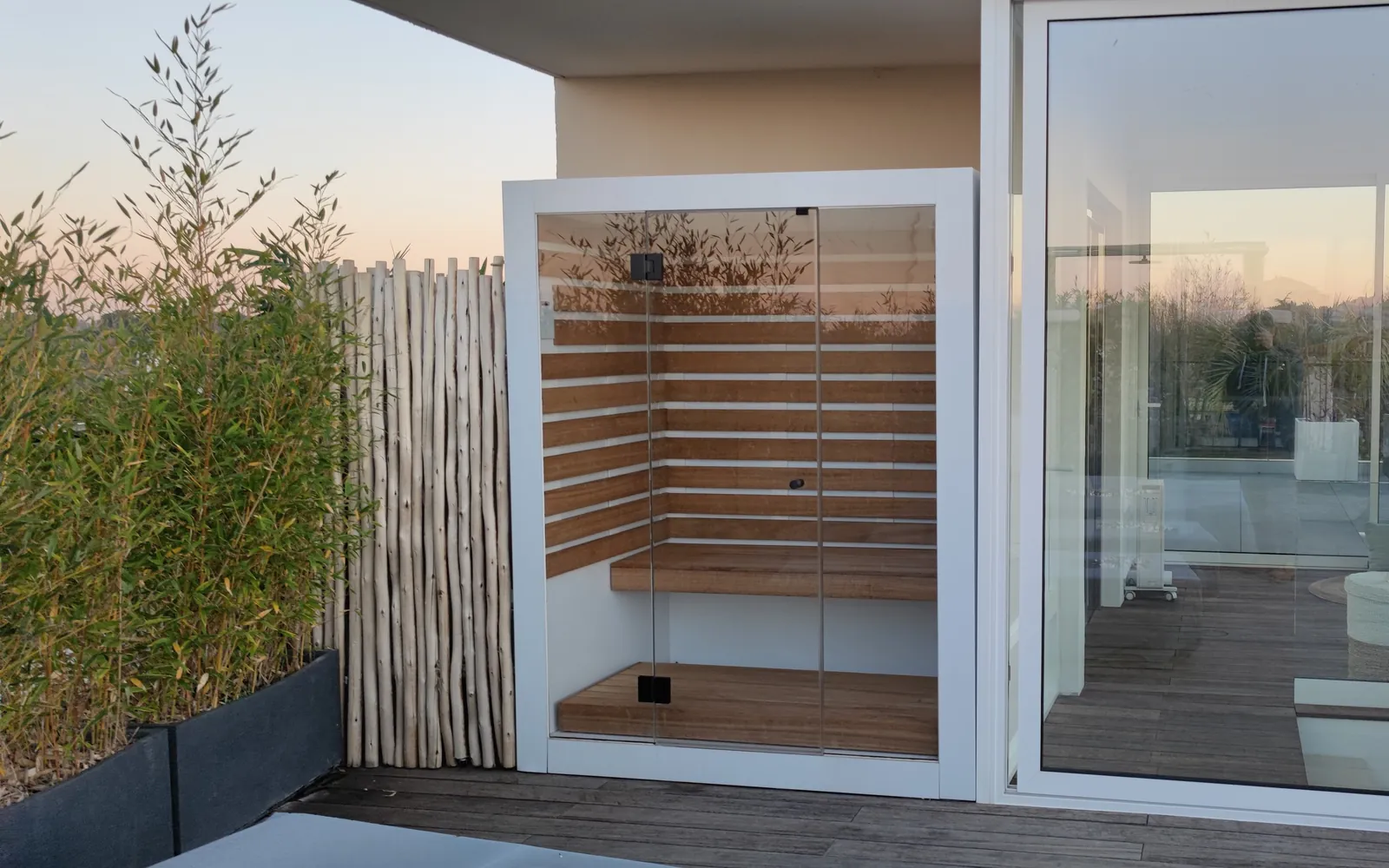 Sauna vitré à cadre blanc posé sur une terrasse en bois au coucher du soleil, à Lattes