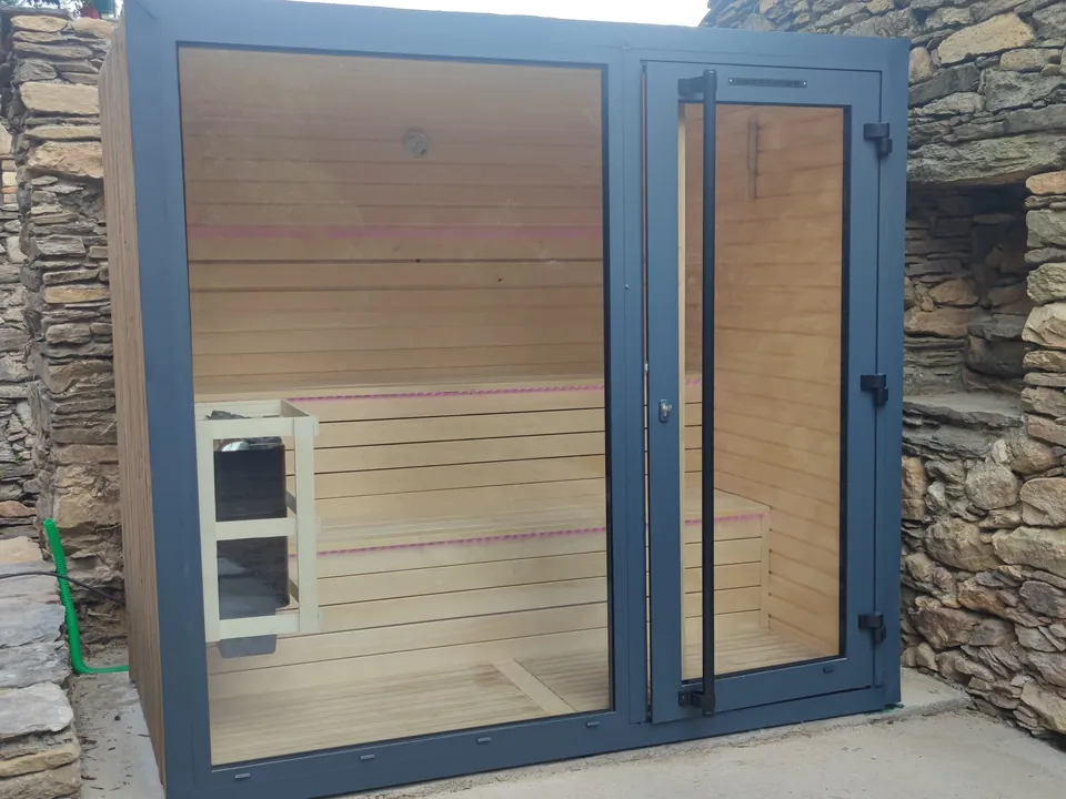 Sauna vitré à cadre anthracite installé dans une cour entre des murs de pierre sèche