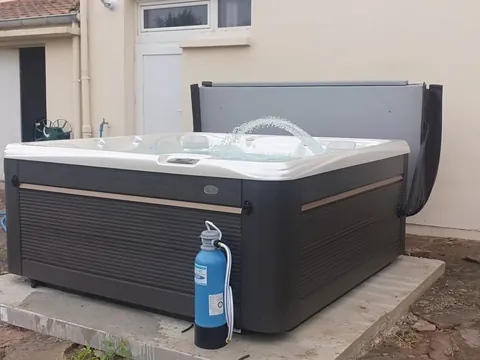 Spa installé sur une dalle devant une façade crépie, couverture relevée