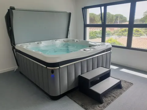 Spa installé en intérieur, devant une baie vitrée, avec son marchepied