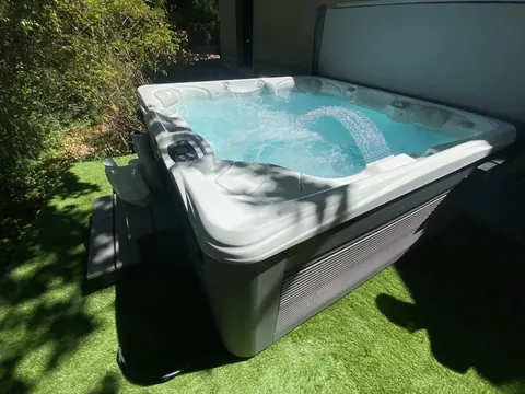 Spa avec jeu d'eau installé sur une pelouse synthétique, au pied d'une haie