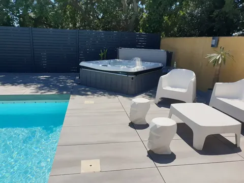 Spa installé au bord d'une piscine, terrasse claire et salon de jardin blanc