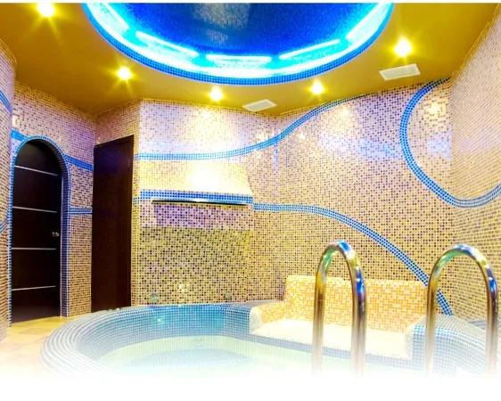 Hammam en mosaïque aux motifs bleus et dorés, arcs, voûte éclairée en bleu et bassin