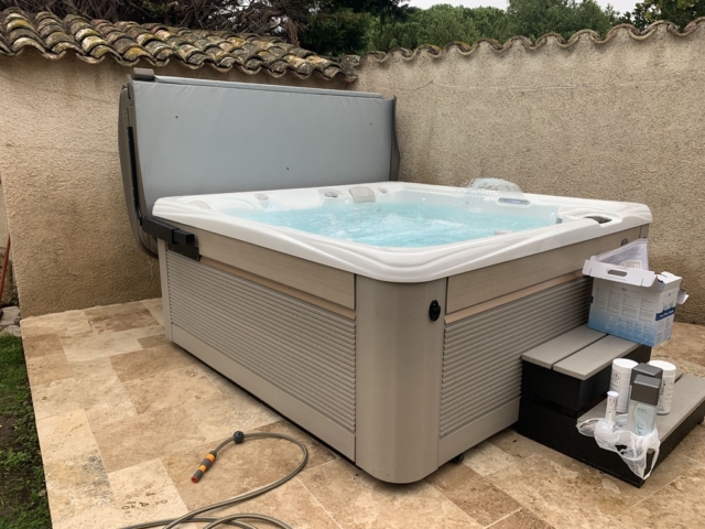 Spa 6 personnes en eau sur une terrasse avec des escaliers et des produits d'entretien